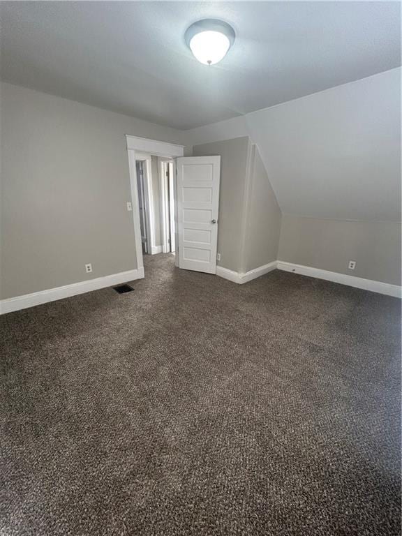 additional living space with dark carpet and vaulted ceiling