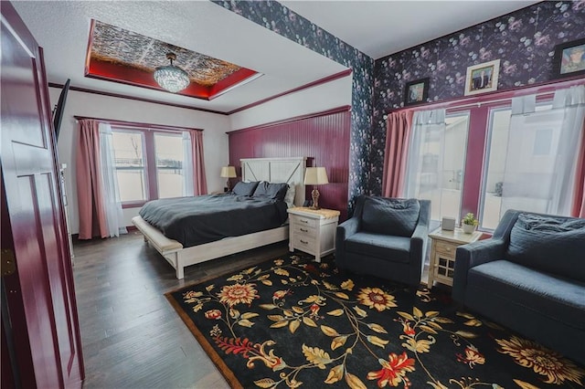 bedroom featuring a raised ceiling, wood finished floors, crown molding, and wallpapered walls