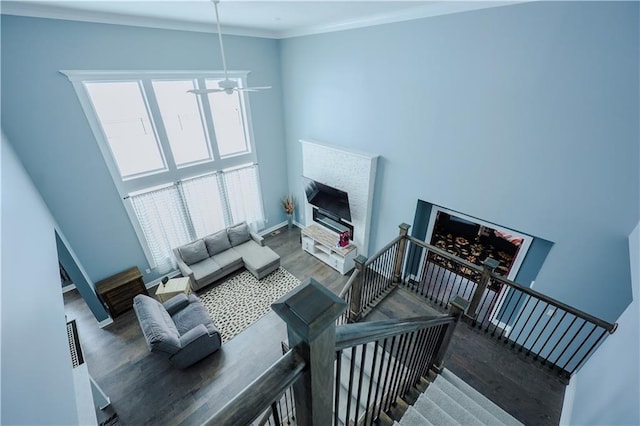 living area with crown molding, baseboards, a fireplace, a high ceiling, and wood finished floors