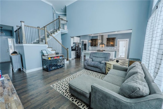 living room featuring dark wood-type flooring, baseboards, stairway, ornamental molding, and a high ceiling