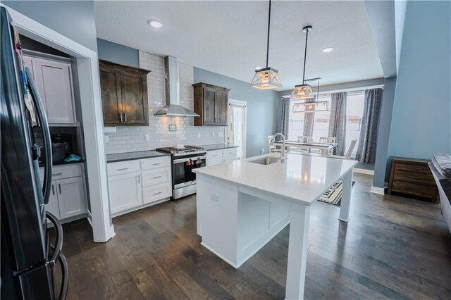 kitchen with backsplash, dark wood finished floors, stainless steel appliances, wall chimney exhaust hood, and a sink