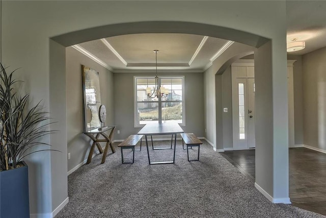 unfurnished dining area with crown molding, a tray ceiling, a chandelier, and dark carpet