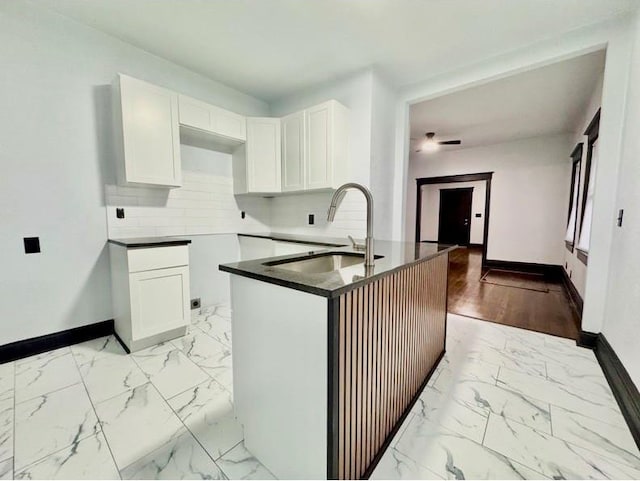 kitchen featuring white cabinets, backsplash, kitchen peninsula, and sink