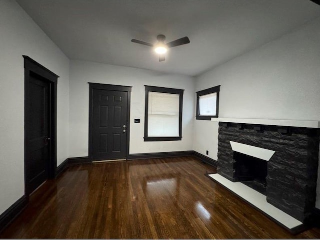 unfurnished living room featuring ceiling fan, dark wood-type flooring, and a stone fireplace