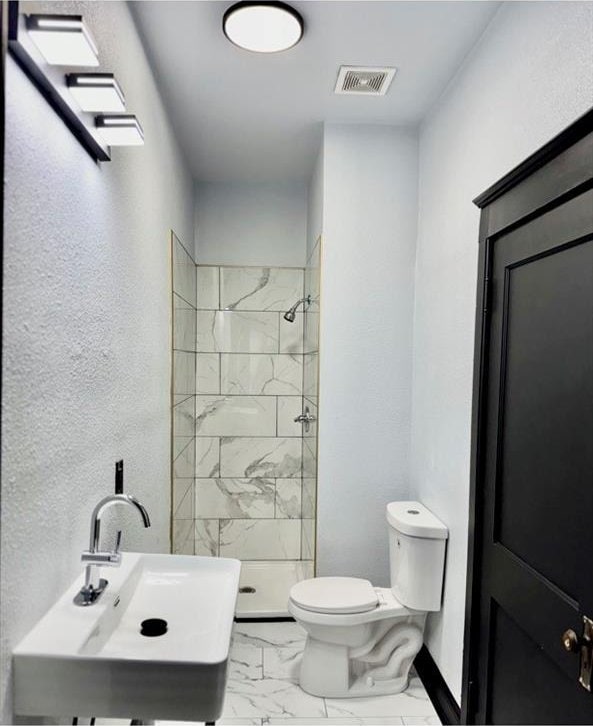 bathroom featuring sink, tiled shower, and toilet