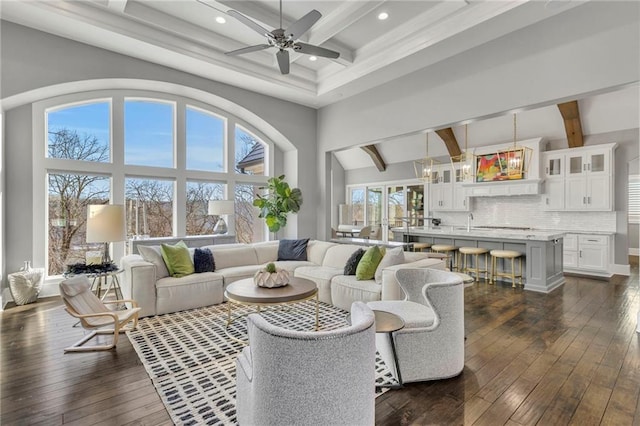 living room with ceiling fan, dark hardwood / wood-style flooring, a high ceiling, and beamed ceiling