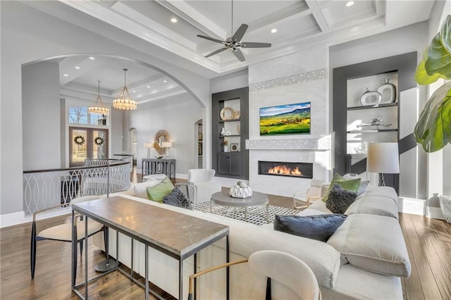 living room with ceiling fan, a fireplace, hardwood / wood-style floors, coffered ceiling, and built in shelves