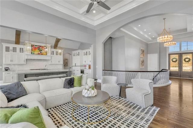 living room featuring dark wood-type flooring, a towering ceiling, beamed ceiling, and ceiling fan with notable chandelier