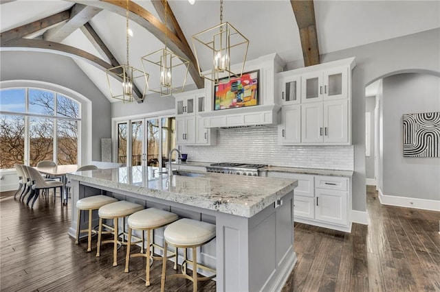 kitchen with an island with sink, tasteful backsplash, decorative light fixtures, white cabinets, and sink