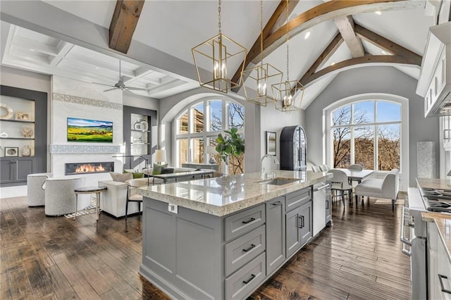 kitchen with decorative light fixtures, a fireplace, a center island with sink, sink, and light stone counters