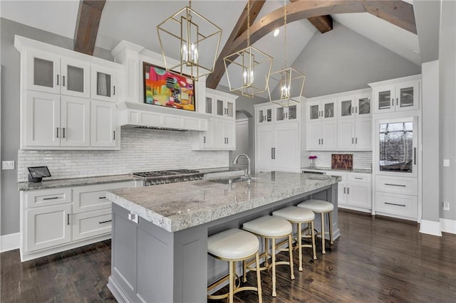 kitchen featuring an island with sink, white cabinets, tasteful backsplash, and beamed ceiling