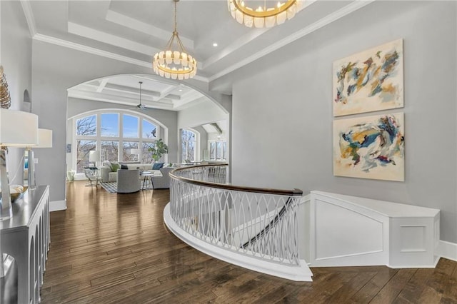 hall with dark wood-type flooring, ornamental molding, a chandelier, and a raised ceiling