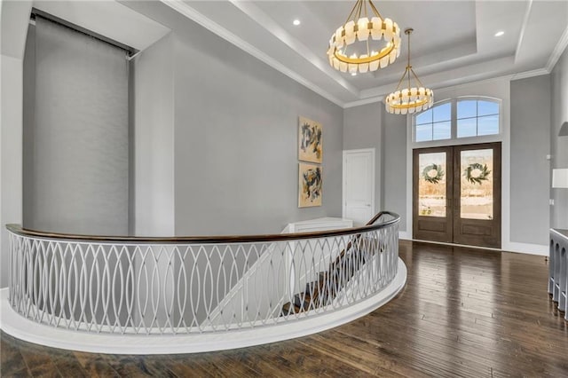 foyer entrance featuring a raised ceiling, dark wood-type flooring, ornamental molding, french doors, and a chandelier