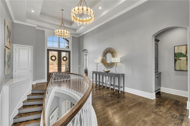 entryway featuring a towering ceiling, french doors, a raised ceiling, a chandelier, and crown molding