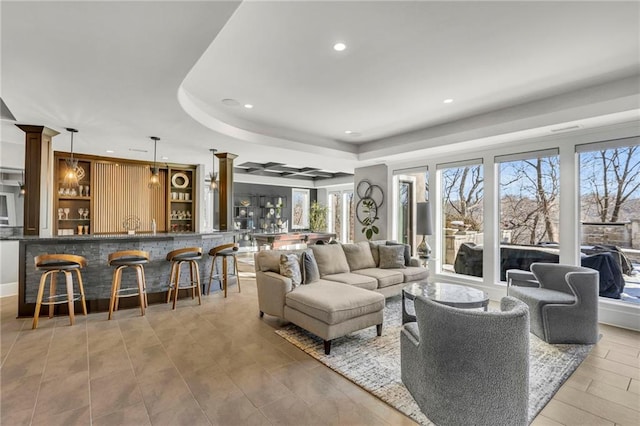 living room featuring a raised ceiling, bar, and decorative columns