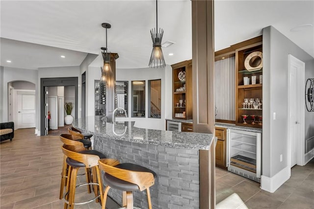 bar with built in features, beverage cooler, light stone counters, and hanging light fixtures