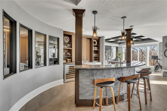 bar with pendant lighting, built in shelves, stone counters, and wine cooler