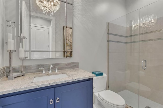 bathroom featuring toilet, an inviting chandelier, a shower with shower door, tasteful backsplash, and vanity