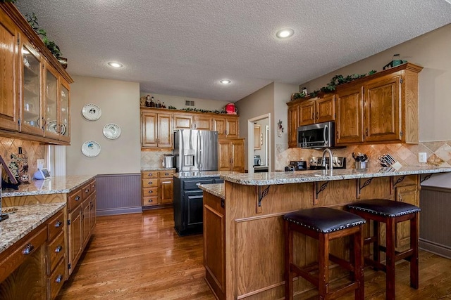 kitchen featuring stainless steel appliances, light stone countertops, backsplash, and hardwood / wood-style floors