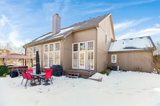 snow covered back of property with a hot tub and central AC