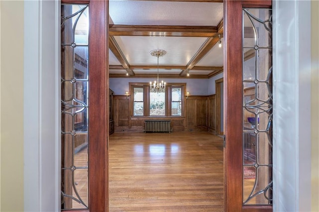 spare room with radiator, light hardwood / wood-style flooring, an inviting chandelier, coffered ceiling, and beamed ceiling