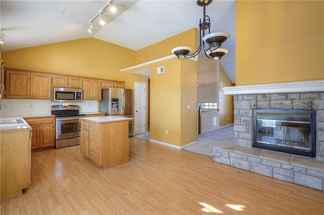 kitchen with a kitchen island, lofted ceiling, backsplash, appliances with stainless steel finishes, and a stone fireplace