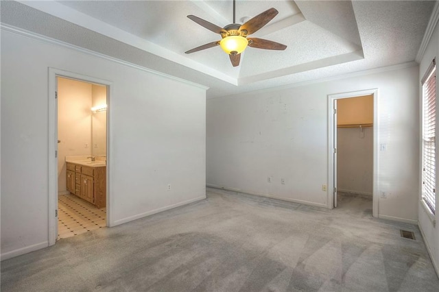 unfurnished bedroom featuring ornamental molding, a raised ceiling, connected bathroom, a walk in closet, and ceiling fan