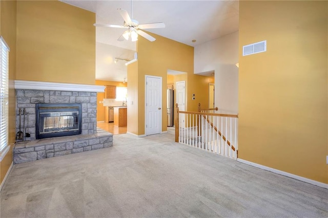 unfurnished living room featuring ceiling fan, high vaulted ceiling, a stone fireplace, and light carpet