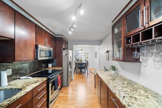 kitchen with tasteful backsplash, light hardwood / wood-style floors, appliances with stainless steel finishes, track lighting, and light stone counters