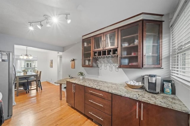 kitchen featuring stainless steel fridge, a notable chandelier, light wood-type flooring, decorative light fixtures, and light stone counters