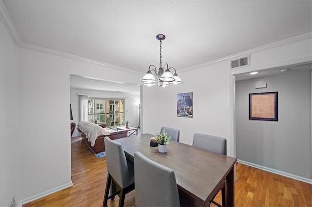 dining area featuring light hardwood / wood-style floors, a textured ceiling, crown molding, and a notable chandelier