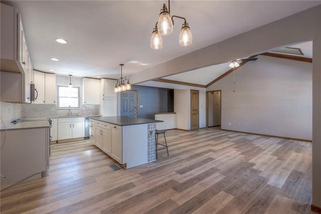 kitchen with white cabinets, lofted ceiling, a kitchen island, sink, and hanging light fixtures