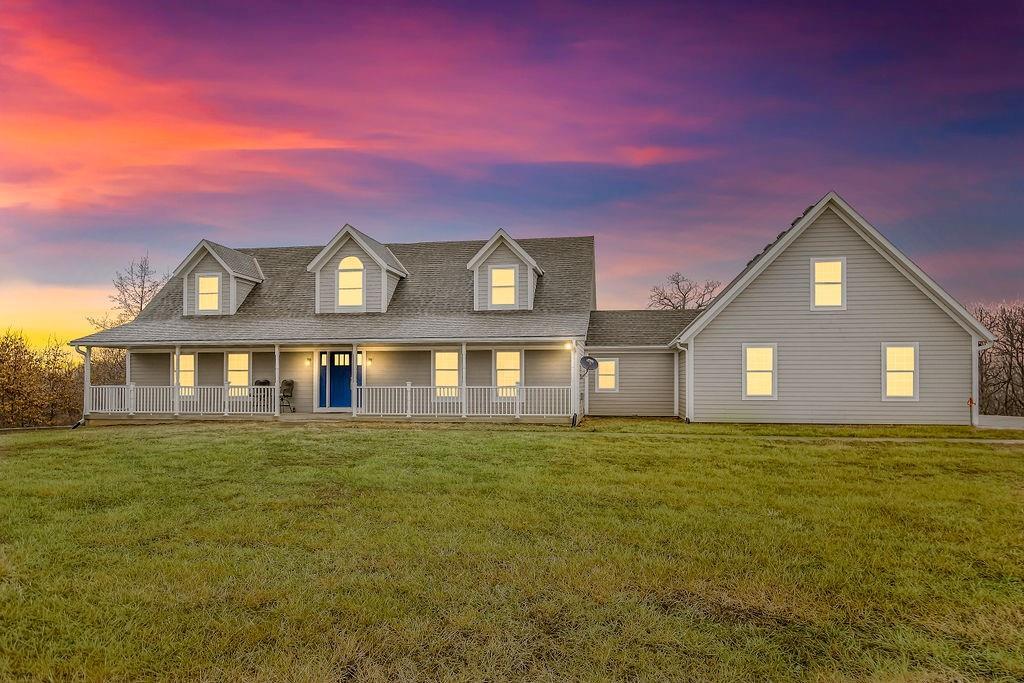 cape cod house with a yard and covered porch