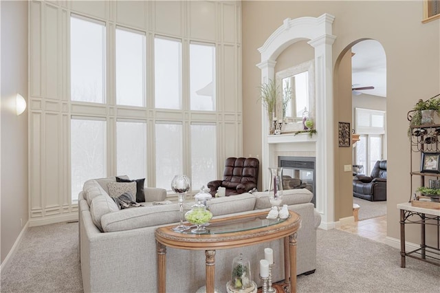 carpeted living room with a towering ceiling, ceiling fan, and ornate columns