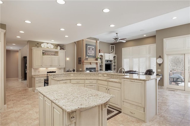 kitchen with sink, light stone counters, cream cabinets, ceiling fan, and a kitchen island with sink