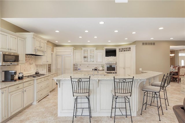 kitchen featuring light stone countertops, stainless steel appliances, a kitchen bar, and a center island with sink