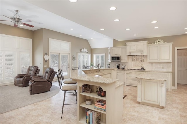 kitchen with light stone counters, cream cabinets, stainless steel appliances, a kitchen island with sink, and a breakfast bar area