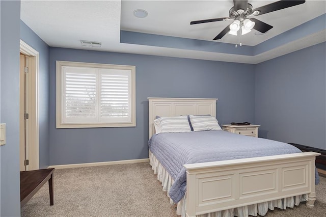 bedroom featuring ceiling fan, a tray ceiling, and light carpet