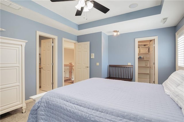 bedroom with a closet, light colored carpet, ceiling fan, a tray ceiling, and a walk in closet