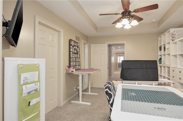 carpeted home office featuring ceiling fan and a raised ceiling