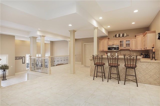 kitchen featuring light brown cabinets, light tile patterned flooring, a kitchen bar, kitchen peninsula, and backsplash