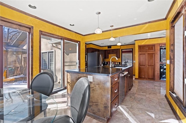 kitchen featuring pendant lighting, sink, ornamental molding, stainless steel appliances, and a center island with sink