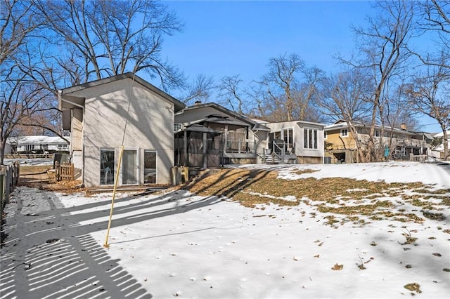 snow covered rear of property featuring a sunroom