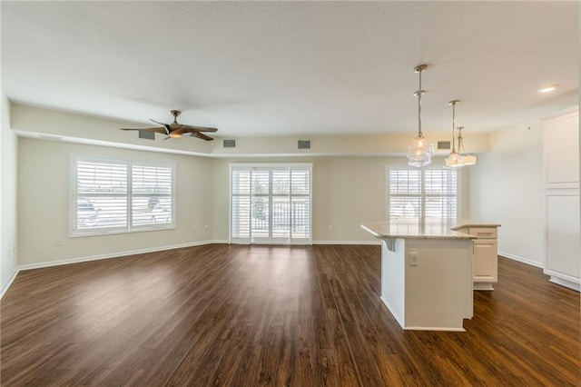 kitchen featuring decorative light fixtures, ceiling fan with notable chandelier, a center island, white cabinets, and light stone counters