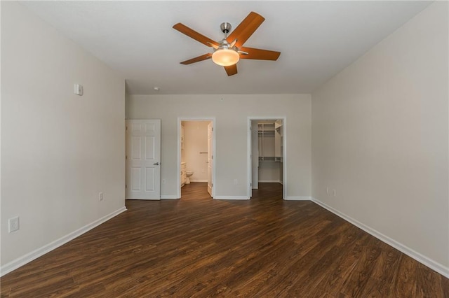 unfurnished bedroom featuring ceiling fan, ensuite bath, dark wood-type flooring, a walk in closet, and a closet