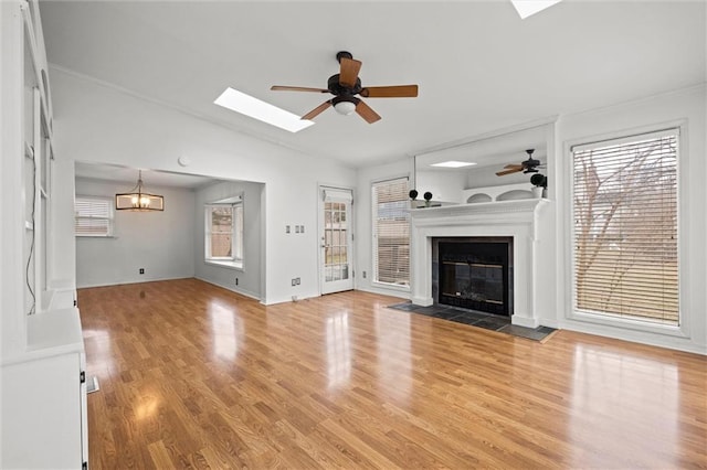 unfurnished living room with ceiling fan with notable chandelier, lofted ceiling with skylight, and light hardwood / wood-style floors