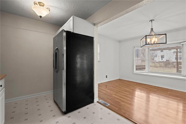 kitchen featuring stainless steel fridge, hanging light fixtures, a textured ceiling, white cabinets, and a chandelier