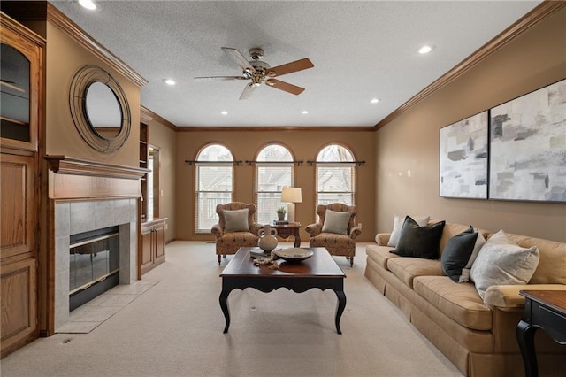 living room featuring light carpet, a textured ceiling, ornamental molding, a tile fireplace, and ceiling fan