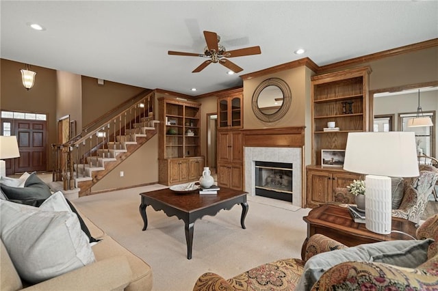 carpeted living room featuring a tiled fireplace, crown molding, ceiling fan, and built in shelves