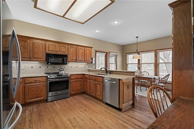 kitchen with sink, light wood-type flooring, kitchen peninsula, pendant lighting, and stainless steel appliances